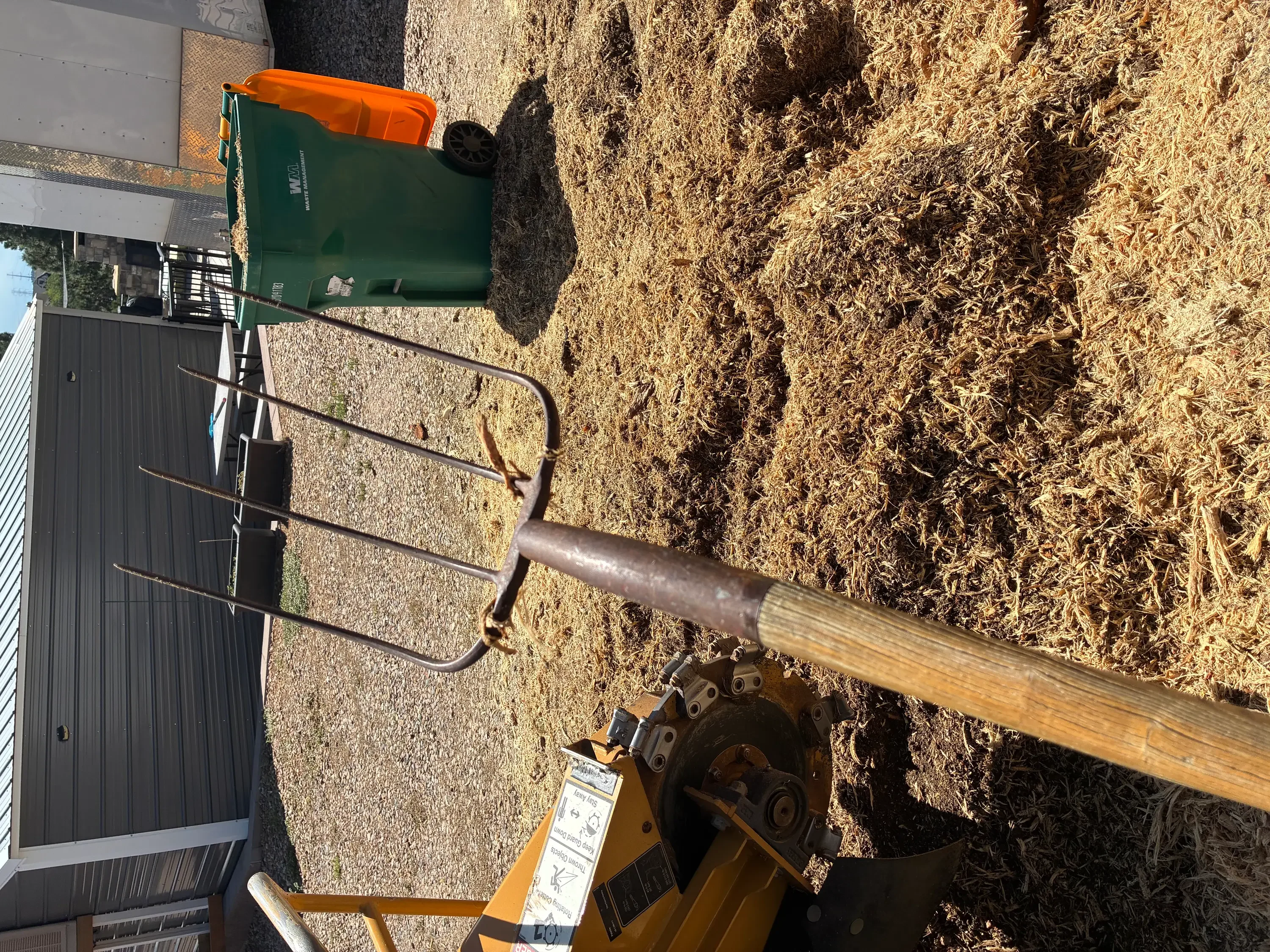 Stump grinder with metal teeth grinding tree stump into wood chips, green waste bin nearby