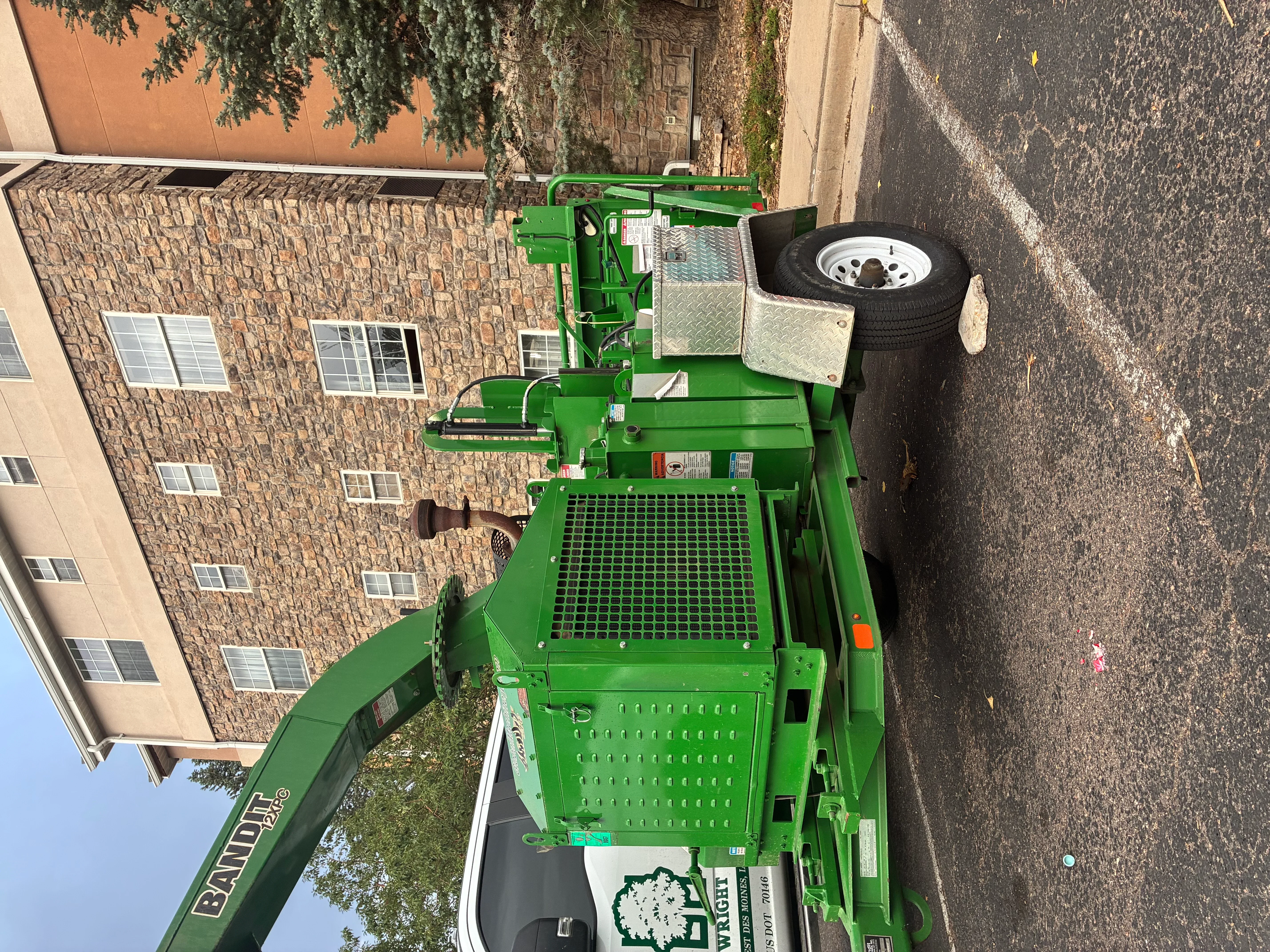 Green hydraulic stump grinder with mesh platform bed and spare tire mounted on trailer