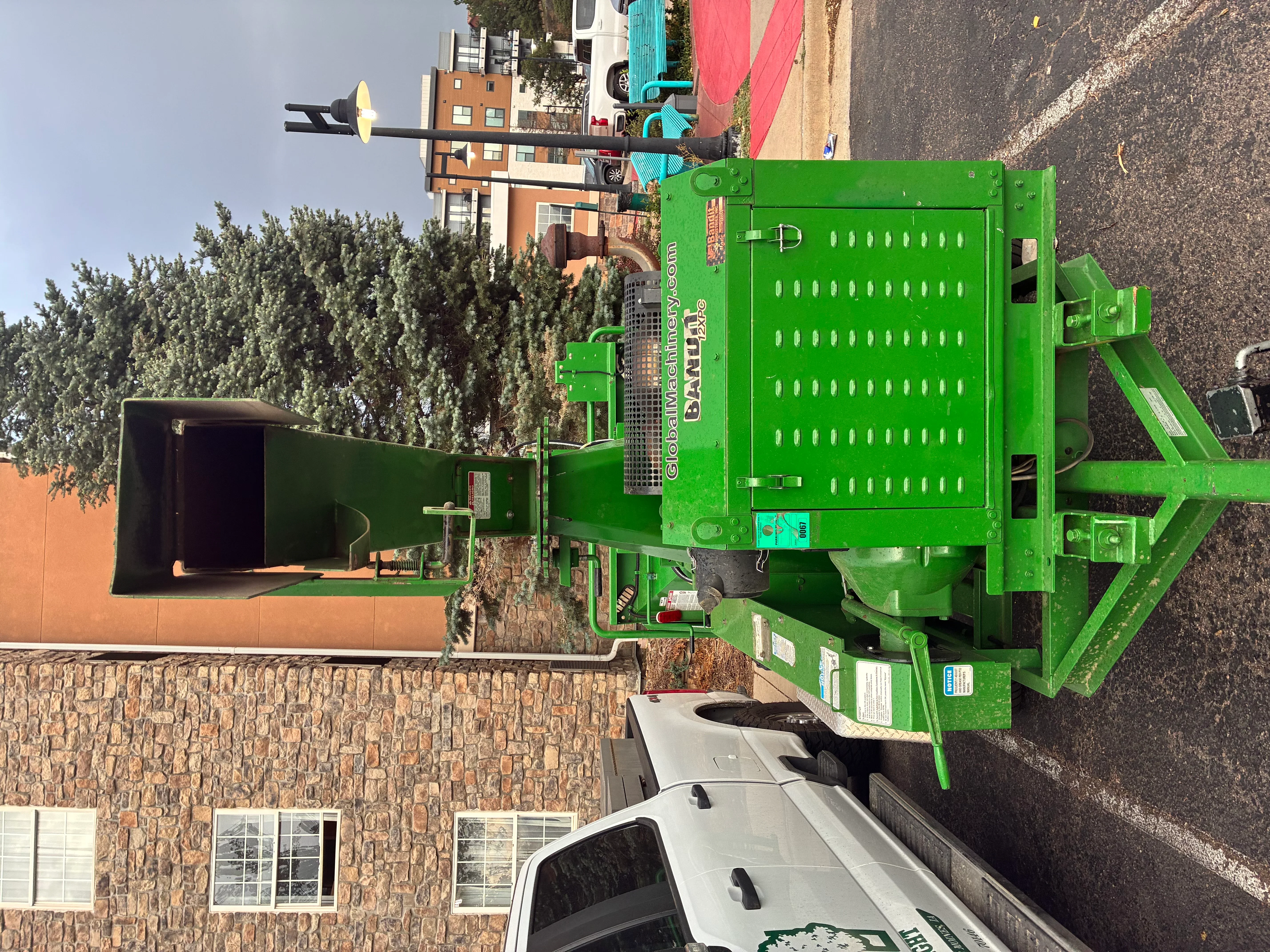 Green hydraulic stump grinder with perforated hopper and boom arm in driveway