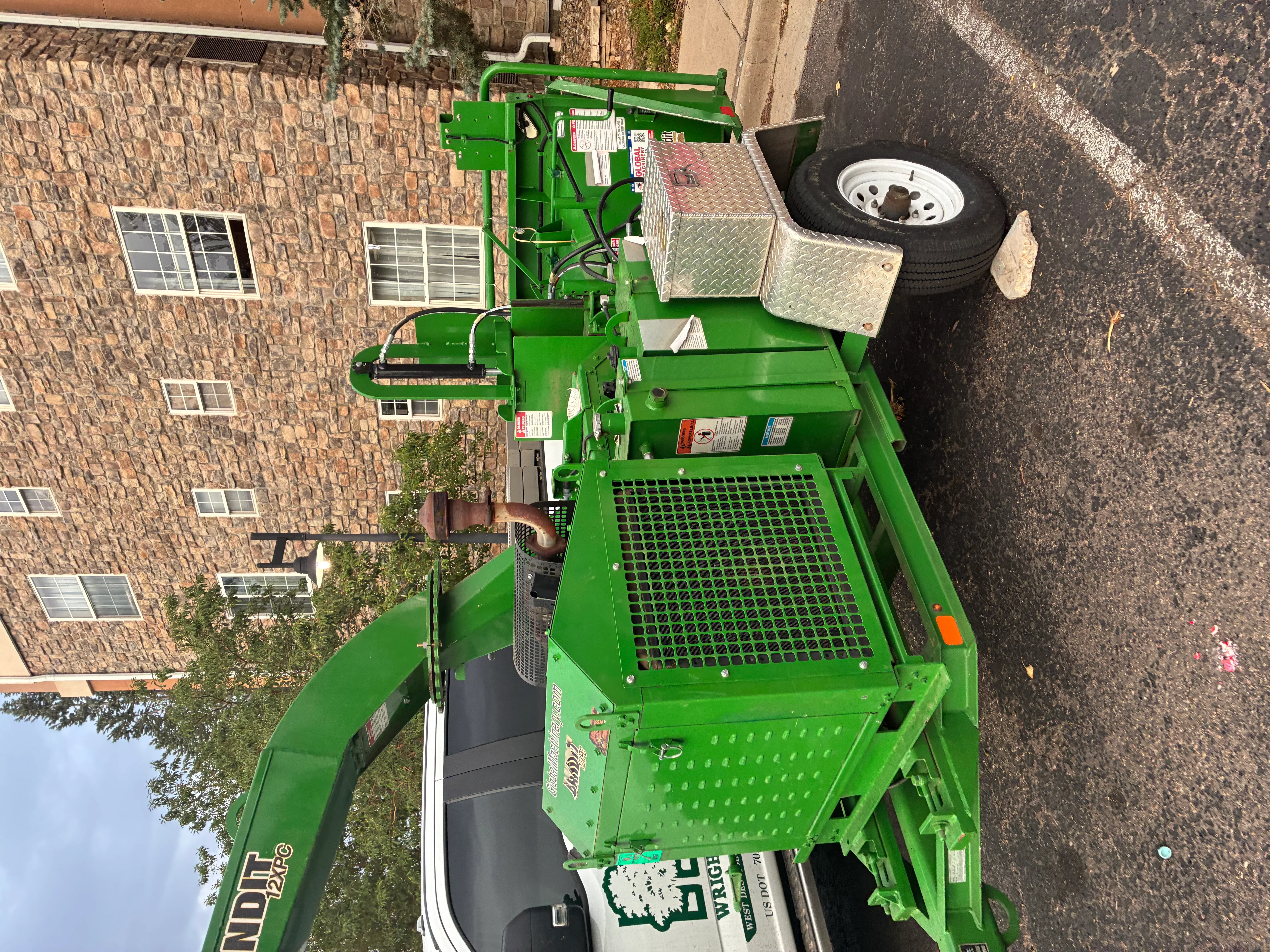 Green hydraulic stump grinder with articulating boom arm and collection basket on trailer