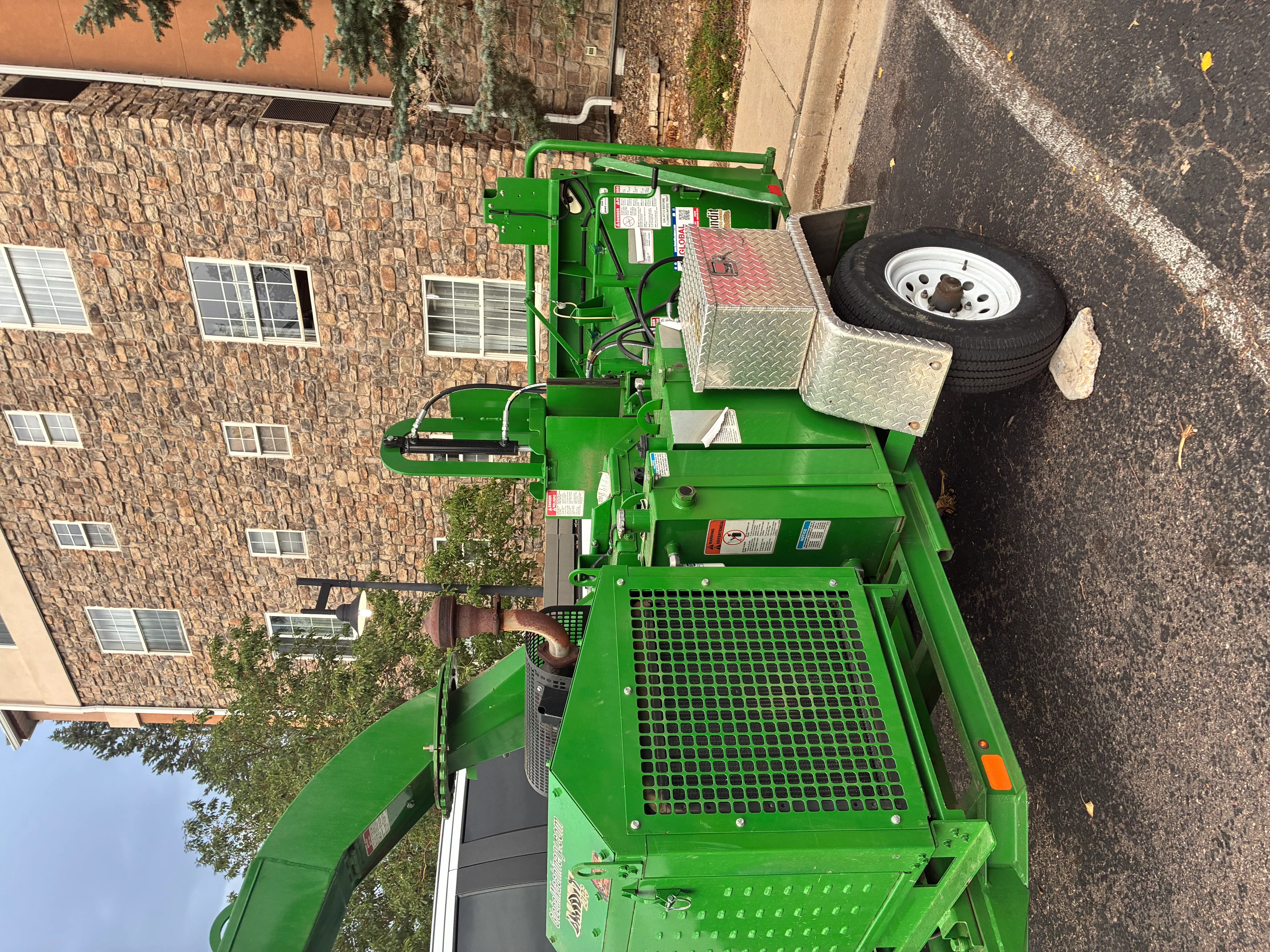 Green stump grinder with hydraulic system and metal grinding head on asphalt driveway