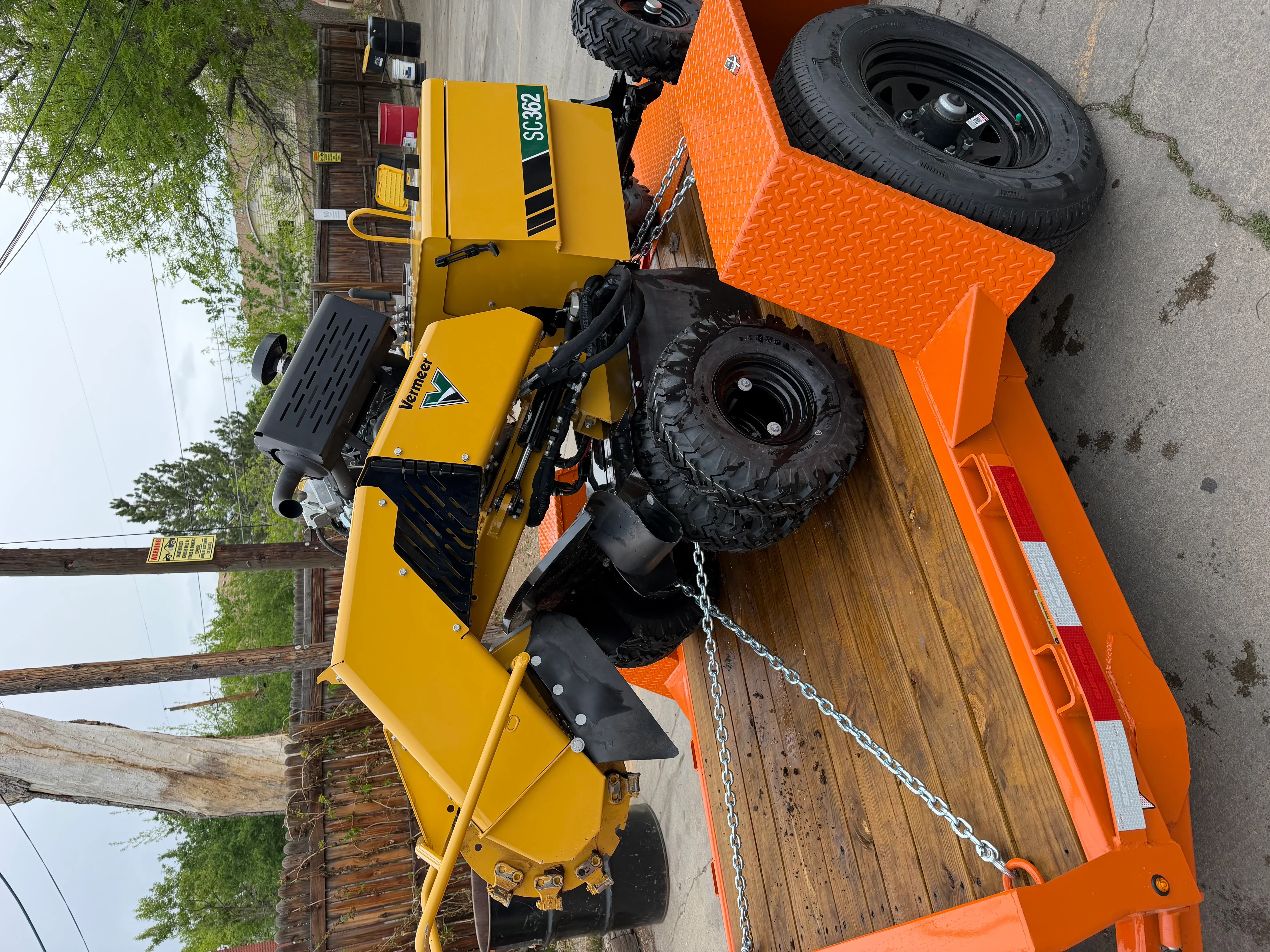 Yellow stump grinder on orange trailer with diamond plate decking and chain securing system