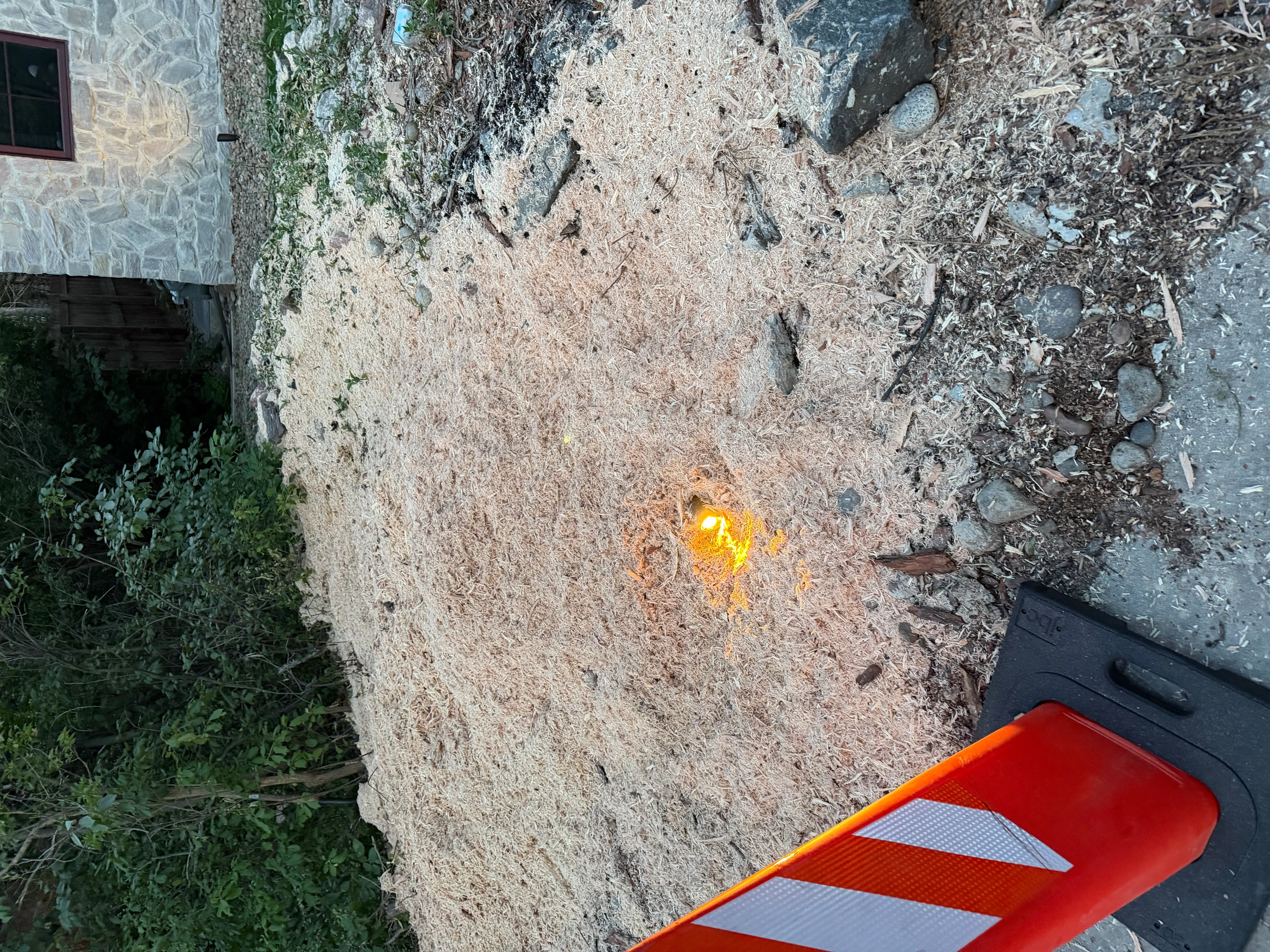 Freshly ground stump area with wood chips and cleared soil, adjacent to stone building foundation